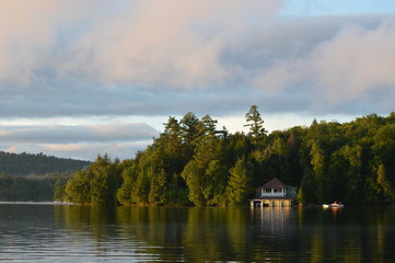 Fototapeta na wymiar Boat house on Saranac Lake bathed in the morning sunrise. The coastline is reflected in the water and framed by the colored clouds