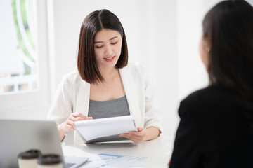 Beautiful asian business woman is reading the resume and gives the interview as a human resource for company recruitment with an interviewee in a white office as a background.