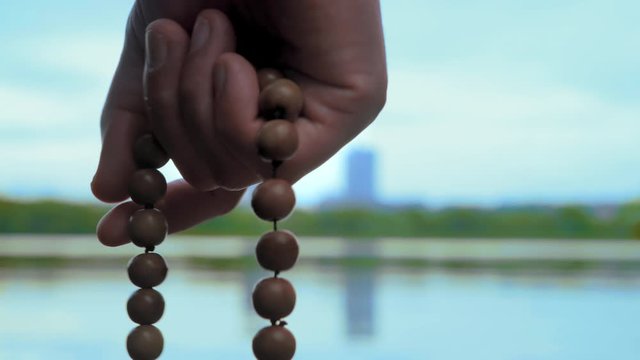 Close-up, Hand of Man with Rosary Reads Prayer on River Background