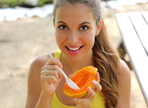 Beautiful brazilian woman eating papaya fruit outdoor.