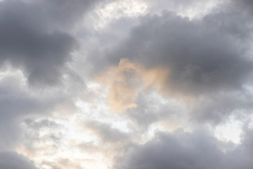 Dark rain clouds. On the clouds you can see a yellow spot from the sunlight. The sun is shining behind the clouds. Overcast weather. Background with free space and empty place.