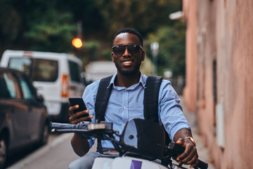 Fototapeta na wymiar Smiling cheerful student on the scooter is waiting for his friend at quaet street.