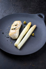 Fried Danish skrei cod fish filet with white asparagus, wasabi and nori as top view on a modern design plate with copy space