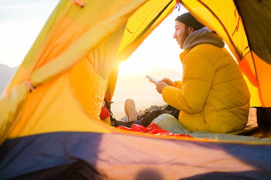the guy in the yellow jacket sits in a tent and enjoys the view of nature and the mountains