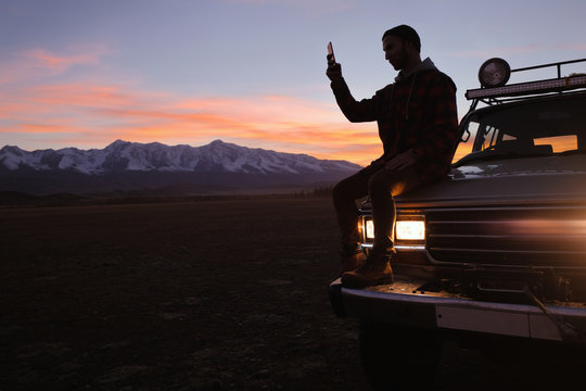 the traveler guy sits on the back of a large jeep and uses the phone
