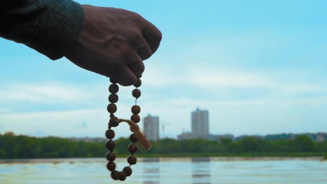 Close-up, Man Holds Wooden Rosary in Hand Standing on River Bank Producing Evening Prayer