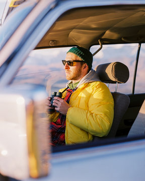 Young hipster guy in sunglasses sits in the car and looks out the window. Travelling by car