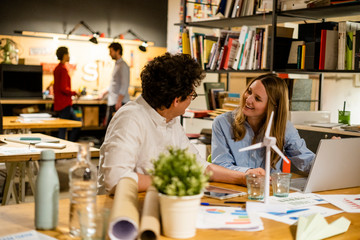 Coworkers working in office with wind turbine model on desk