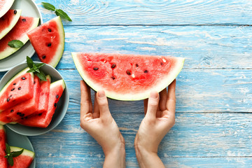   Fresh red watermelon slice in female hands on an blue rustic wood background.  top view. Summer time concept.