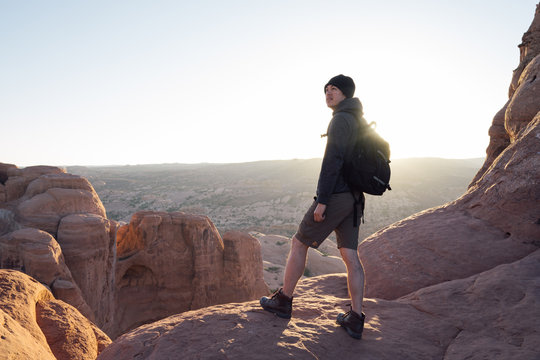 Male hiker pausing to take in the view at sunrise in a rugged desert landscape with beautiful rock formations