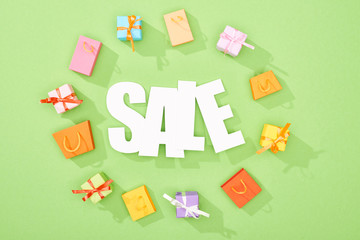 round frame of decorative gift boxes and shopping bags on green background with sale lettering