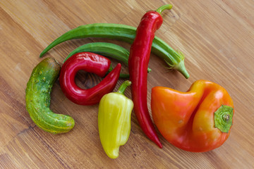 Ordinary and ugly red and green vegetables lie in the center on a brown wooden background, top view