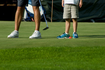 young boy giving a lesson on a golf course green to pull ball into hole, grass, sunset, teacher, sports, concentration, hobby, child, mountain, vacation, Trentino, Alto Adige, Italy