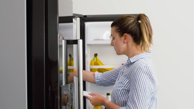 healthy eating and diet concept - woman opening fridge and making list of necessary food at home kitchen