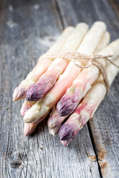 Raw white Asparagus with violet head as bunch on an old rustic wooden board as closeup