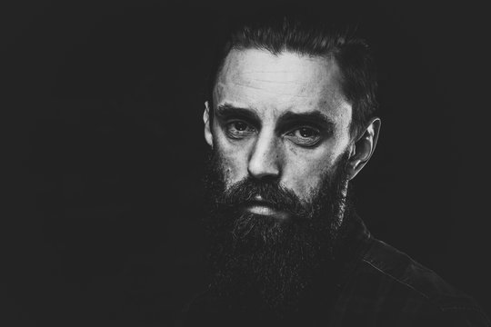 Black and white photo of sad man with beard on the dark background.