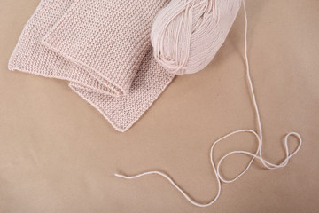A skein of wool and a knitted scarf of beige thread.