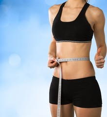 Slim young woman measuring her thin waist with a tape measure, close up