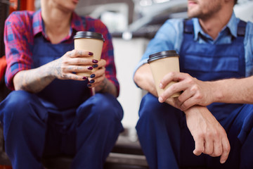 Close up of two automechanics drinking coffee from paper cups.
