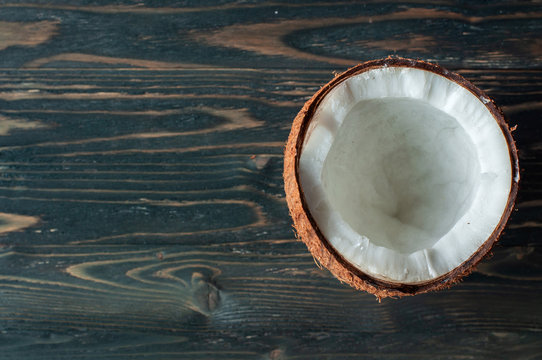 Half a coconut on a black wooden texture background. Copy space