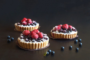 Three delicious tarts, colorful pastry cakes sweets with fresh raspberries and blueberry on black background