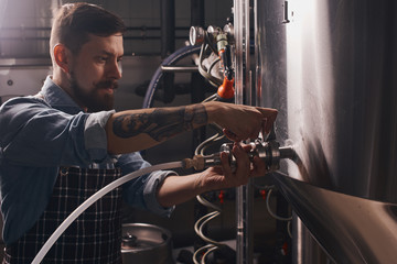 Brewery worker puts on a pipe onto the tap.