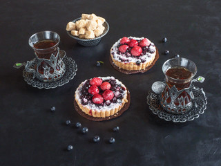 Tea cups, tarts cakes sweets with fresh raspberries and blueberry on black  background