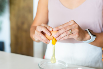 woman cracking egg open over glass bowl