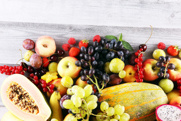 Tropical fruits background, many colorful ripe fruits with strawberries, grapes and cherries on wooden background