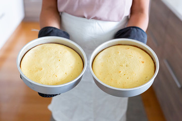 woman holding two baked cakes in metal pans