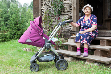 Portrait of elderly woman shaking a baby pram, sitting on porch of country timber house....