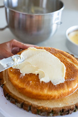 woman icing vanilla cake with metal spatula 
