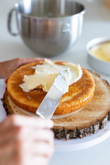 woman icing vanilla cake with metal spatula 