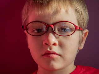 Fototapeta na wymiar Funny child in red sweater on red background actively expresses emotions. Close up little kid boy in glasses posing front of camera