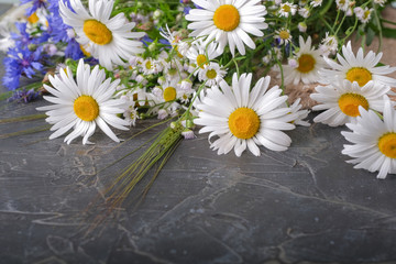 A bouquet of daisies and cornflowers on a dark table.