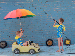 Funny children in boys' bathing suits posing in front of camera with high-pressure car wash and toy...