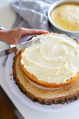woman icing vanilla cake with metal spatula 