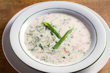 Classic cold soup Okroshka made of vegetables (cucumbers, radishes and spring onions), boiled potatoes, eggs, and meat (beef, sausages or ham)