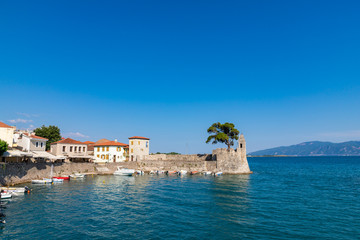 NAFPAKTOS / GREECE - JUNE 27, 2019: View of the port of Nafpaktos with the famous statue and a greek flag