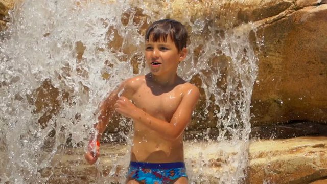 The boy repeats the movement of dance for the coach. Boy is dancing on the rocks on the pool