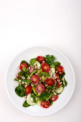 Salad with avocado, cucumbers, cherry tomatoes, spinach leaves, parsley and seeds on a white plate on a white background. Copy space.