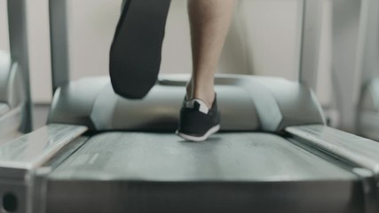 Closeup athletic feet running on treadmill in fitness gym.