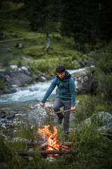 Obraz premium Young man making fire while camping outdoors, in an alpine wilderness