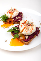 Poached eggs with homemade beetroot hummus, seeds and parsley on toast bread on a white plate on the white background. Healthy breakfast or snack