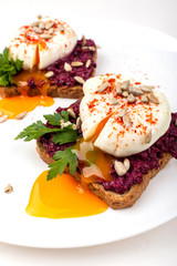 Poached eggs with homemade beetroot hummus, seeds and parsley on toast bread on a white plate on the white background. Healthy breakfast or snack