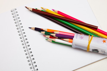 colored pencils wrapped in euro note lie on a white notebook on a white table bright copy space