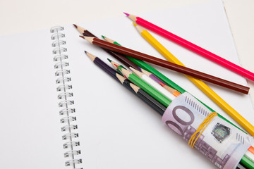 colored pencils wrapped in euro note lie on a white notebook on a white table bright copy space