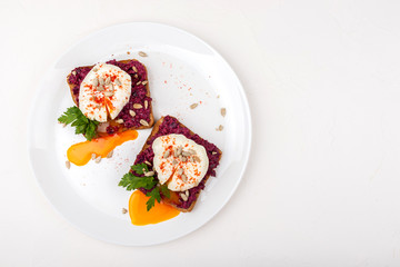 Poached eggs with homemade beetroot hummus, seeds and parsley on toast bread on a white plate on the white background. Healthy breakfast or snack. Copy space