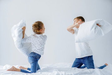 Naughty twins girl and boy friendly fighting staged a pillow fight on the bed in the bedroom. They...