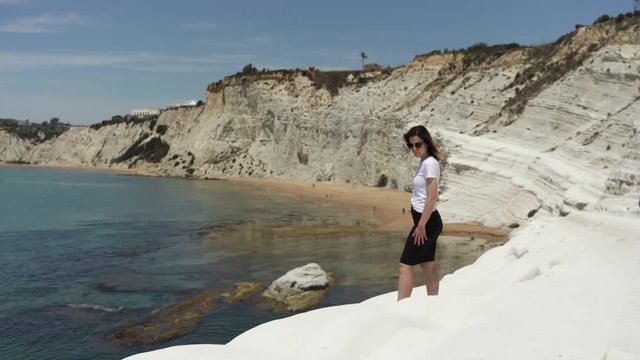 Woman sits on white rock cliff Scala dei Turchi by sea coastline in Sicily